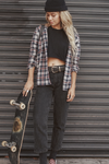 Gal holding a skateboard against a metallic shutter background in the Stellar moto brand Utopia riding and extreme sports Jeans