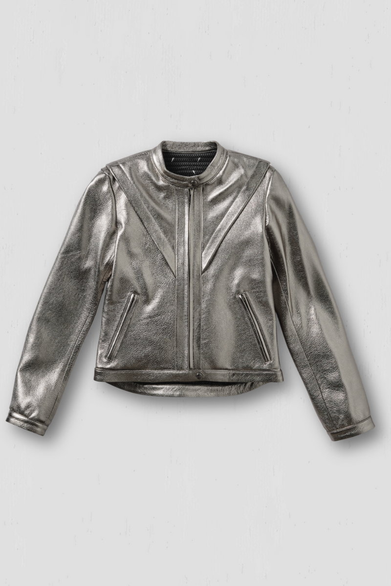 A woman standing in a shop wearing a silver leather motorcycle jacket with armor, sunglasses, and a cap.